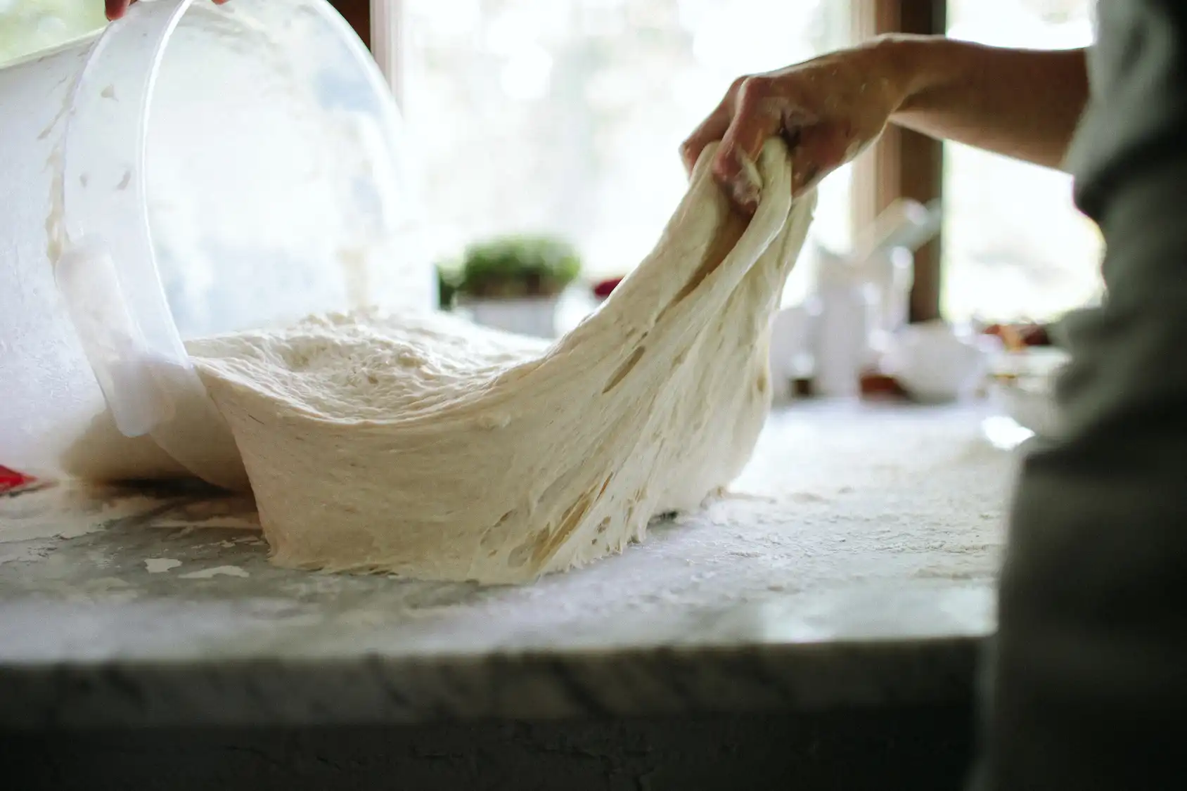 Prodotti lasciati lievitare a lungo, per migliorare digeribilità e gusto e lasciare il giusto tempo di fermentazione. Una persona impasta a mano un impasto.