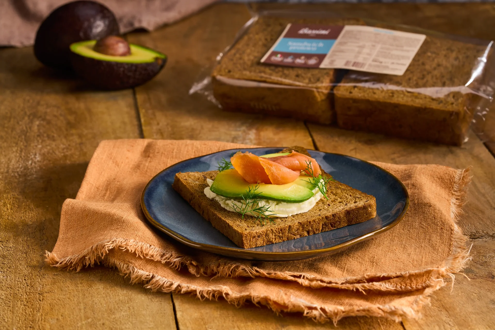 Sandwich proteico Bassini 1963 farcito con crema di formaggio, fettine d'avocado, salmone affumicato e ciuffetti di erba cipollina. Un prodotto gustoso e nutriente.